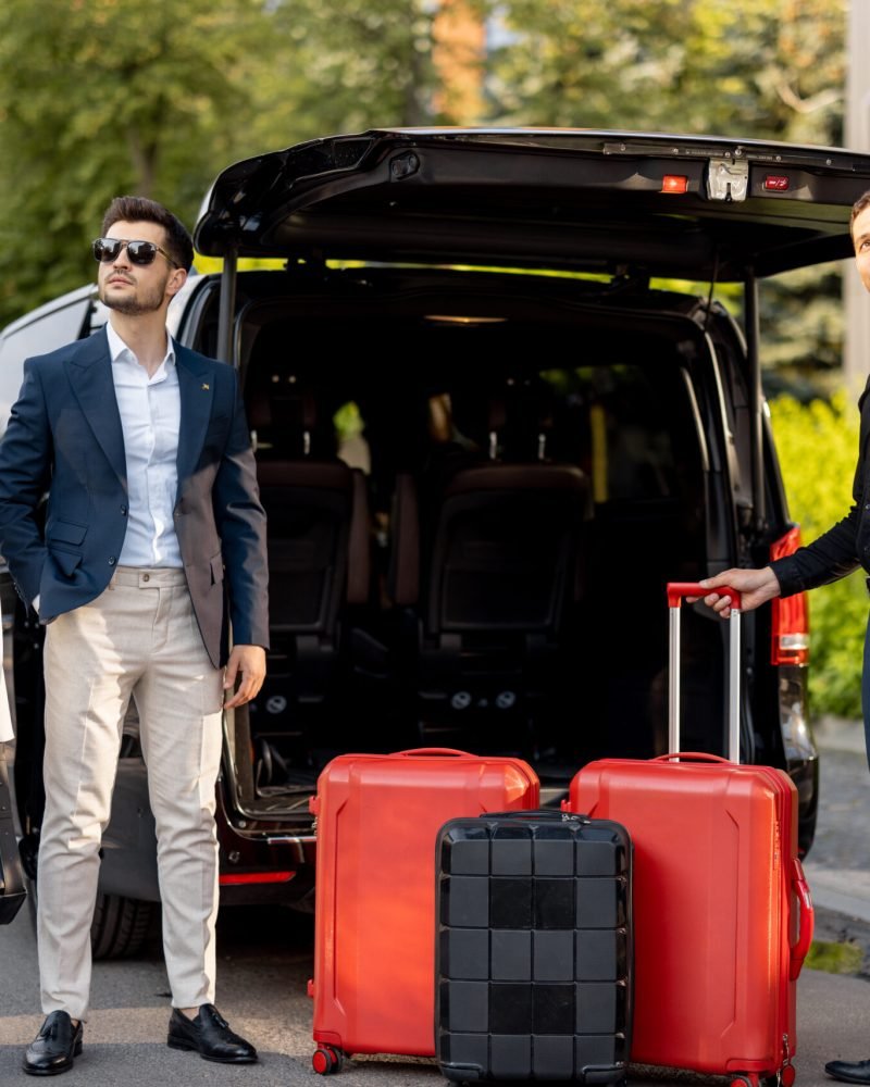 Business couple standing by a minivan taxi waiting for their chauffeur or porter to help them with a suitcases. Concept of business trips and travel