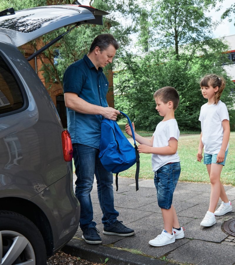 Dad, father sees off, leads the children to school, brother and sister, boy and girl, takes backpacks out of the car. School days, the beginning of the school day.